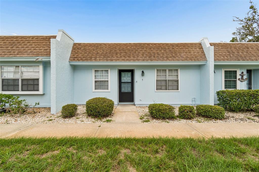 A light blue, single-story townhouse exterior features a brown shingled roof and a front walkway — 11110 CARRIAGE HILL DRIVE UNIT 5, PORT RICHEY, FL