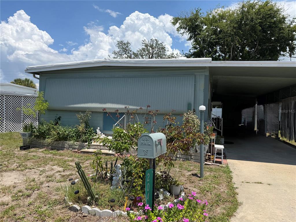 A light-colored mobile home features a concrete driveway, a carport, and a landscaped front yard — 2044 HOYLE DRIVE, HOLIDAY, FL