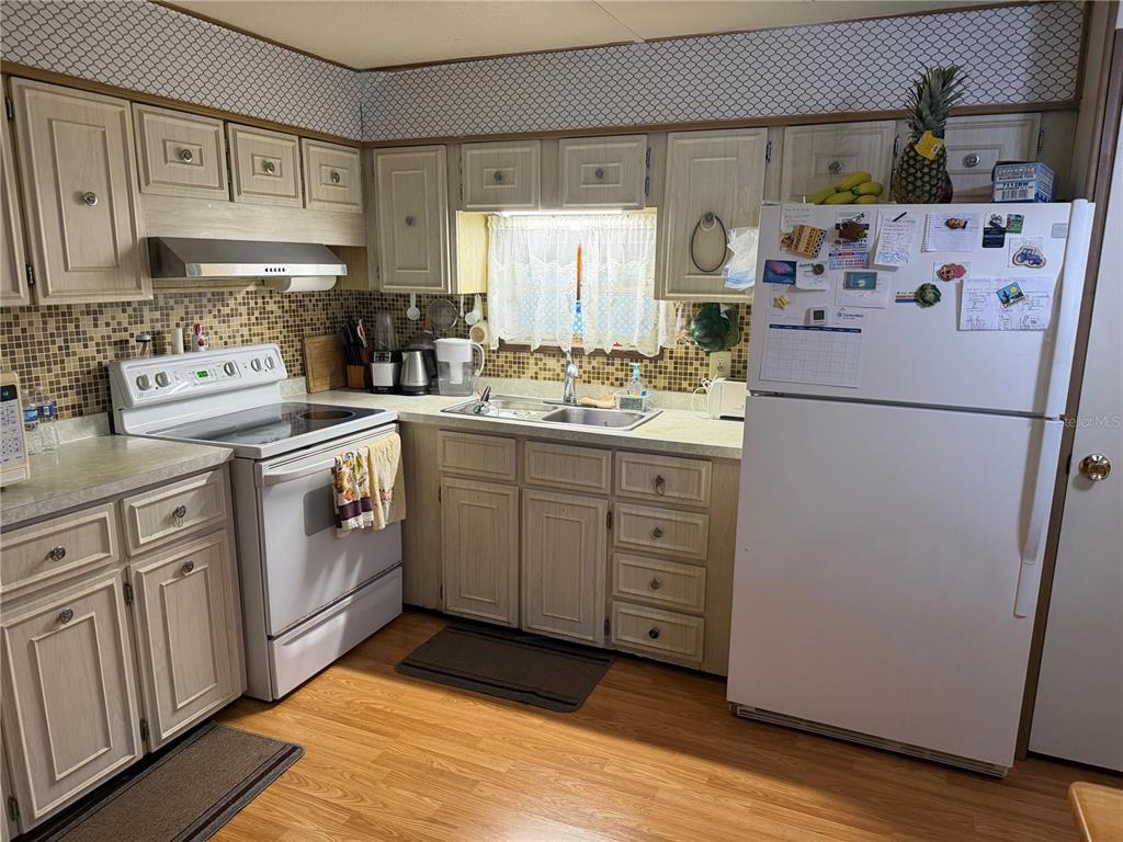 A kitchen features light wood cabinets, a white stove, a white refrigerator, and mosaic backsplash — 2044 HOYLE DRIVE, HOLIDAY, FL