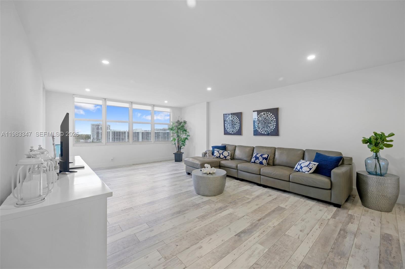 A living room features light wood-look flooring, a grey sectional sofa, and large windows — 3725 S Ocean Dr # 924, Hollywood FL 33019, HOLLYWOOD, FL