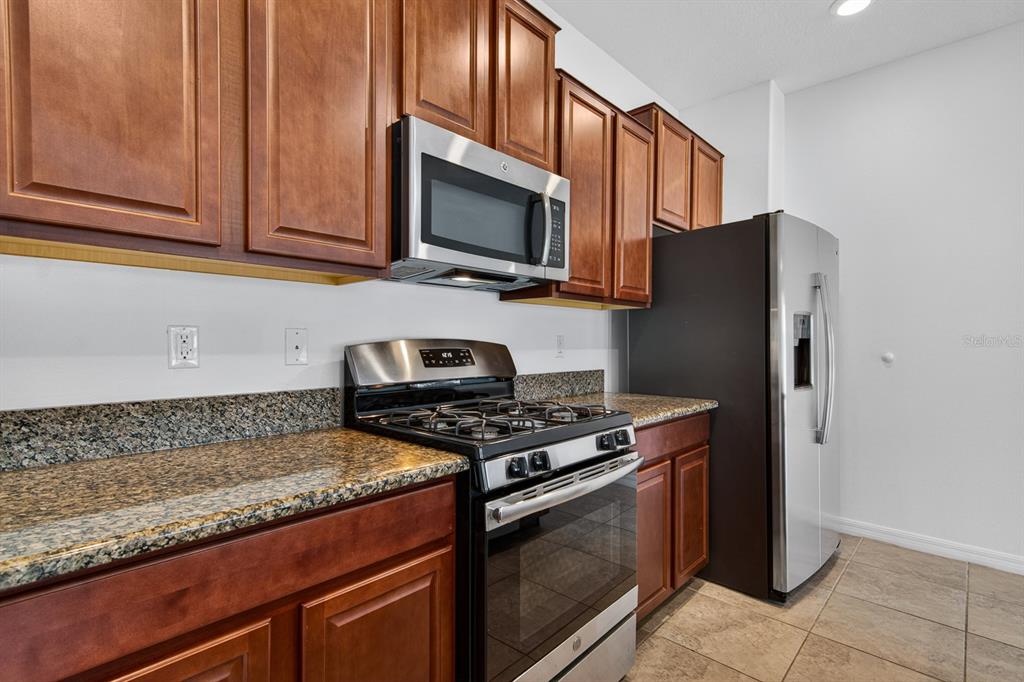 A kitchen features wood cabinets, granite countertops, and stainless steel appliances — 3488 PINE RIBBON DRIVE, LAND O LAKES, FL