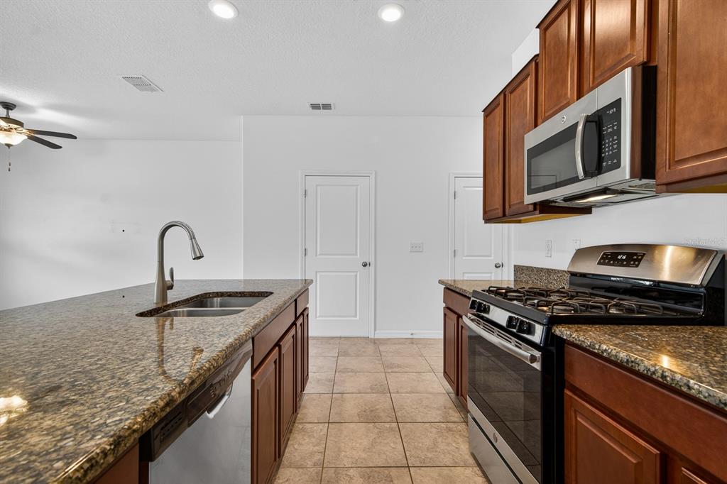 A kitchen features dark wood cabinets, granite countertops, stainless steel appliances, and tile flooring — 3488 PINE RIBBON DRIVE, LAND O LAKES, FL