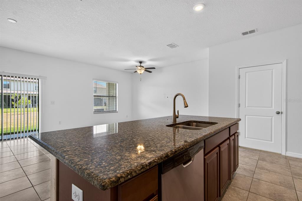 A kitchen island with a granite countertop and stainless steel sink faces a living area — 3488 PINE RIBBON DRIVE, LAND O LAKES, FL