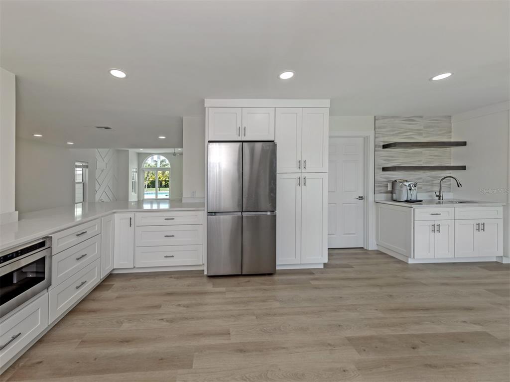 A modern kitchen features white cabinetry, stainless steel appliances, light wood flooring, and a wet bar — 212 SUNRISE DRIVE, NOKOMIS, FL