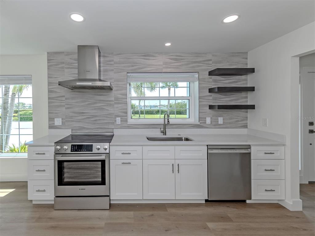 A modern kitchen features white cabinets, stainless steel appliances, and a textured gray tile backsplash — 212 SUNRISE DRIVE, NOKOMIS, FL