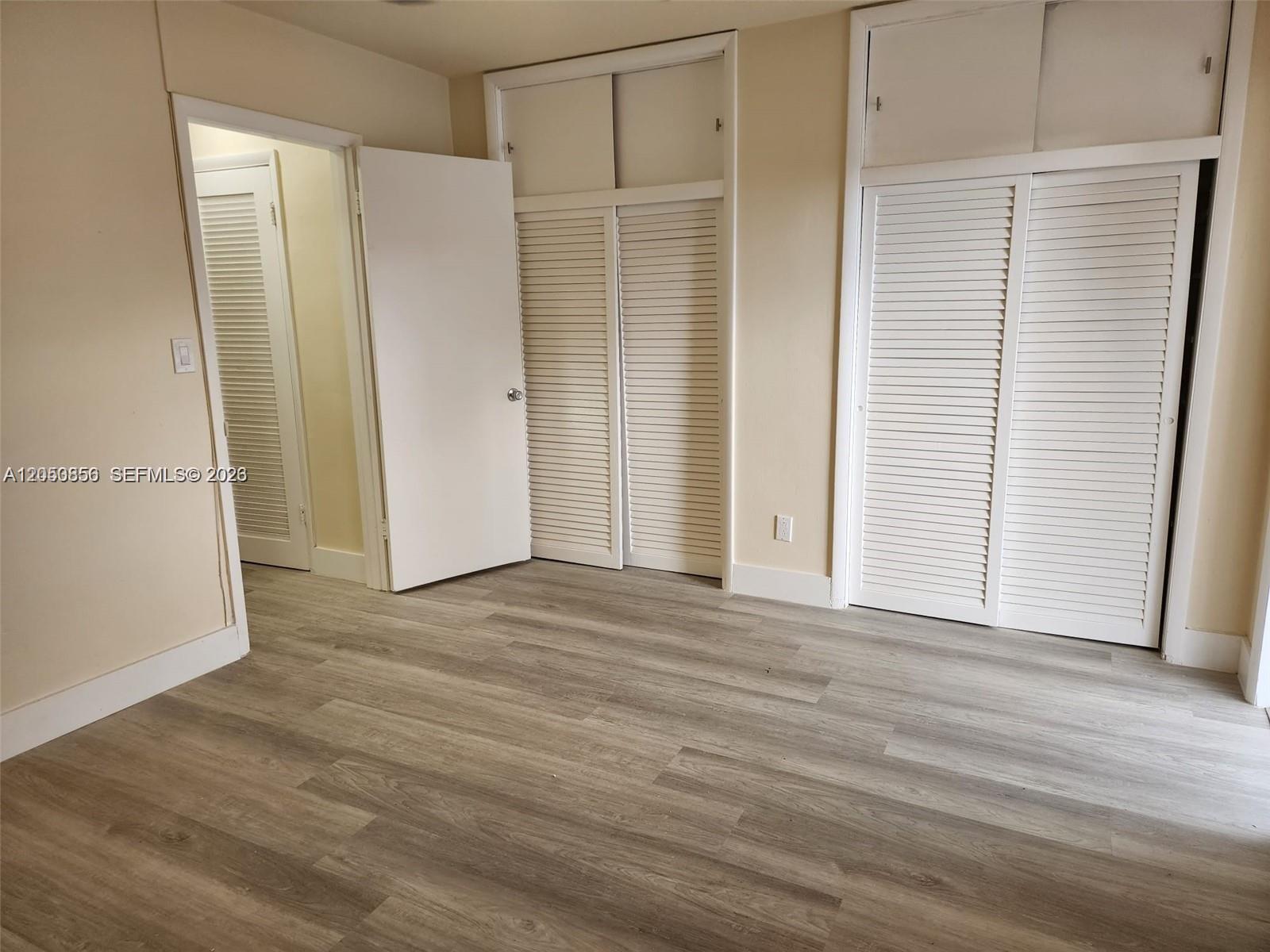 A room features light-colored wood-look flooring, beige walls, and two sets of white louvered closet doors — HOLLYWOOD, FL