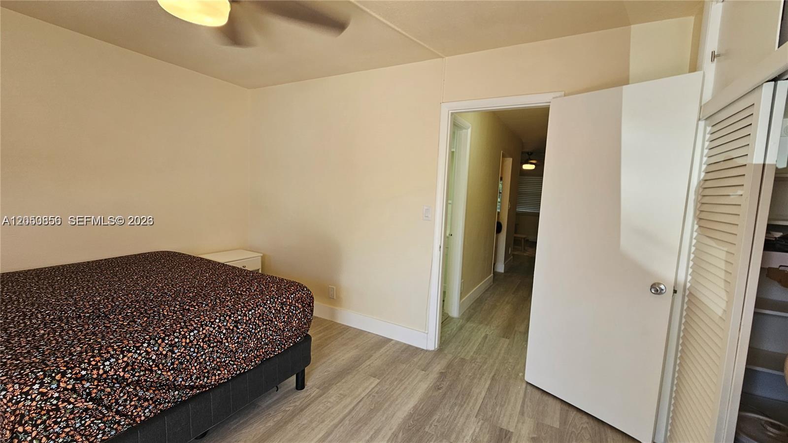 A bedroom features a bed, light-colored walls, wood-look flooring, and an open closet door — HOLLYWOOD, FL
