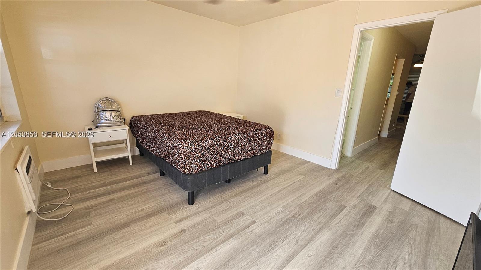 A bedroom features light-colored walls, wood-look flooring, a bed with a patterned comforter, and a doorway — HOLLYWOOD, FL