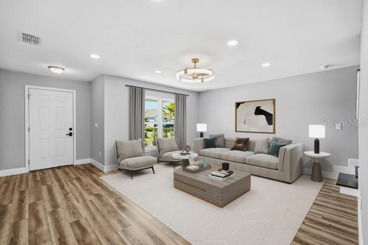 A living room features light gray walls, wood-look flooring, a beige area rug, and furniture — 728 BELVOIR DRIVE, DAVENPORT, FL
