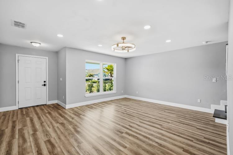 An empty living room features light gray walls, wood-look flooring, a ceiling fan, and a door — 728 BELVOIR DRIVE, DAVENPORT, FL