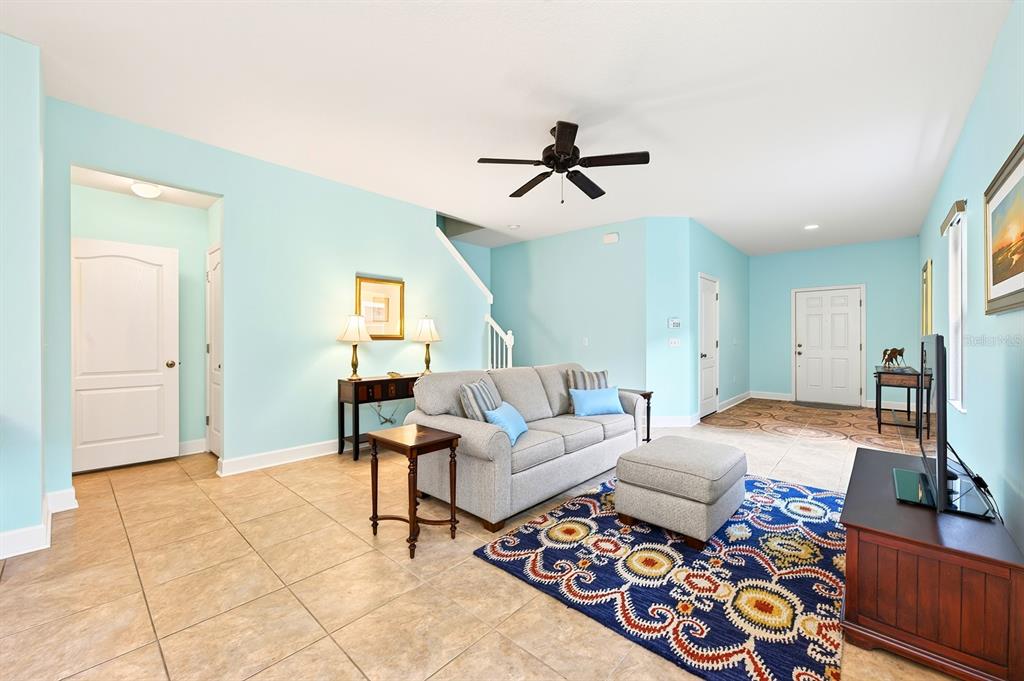 A living room with light blue walls, tile flooring, a gray sofa, and patterned rug — 5585 RUTHERFORD PLACE, OVIEDO, FL