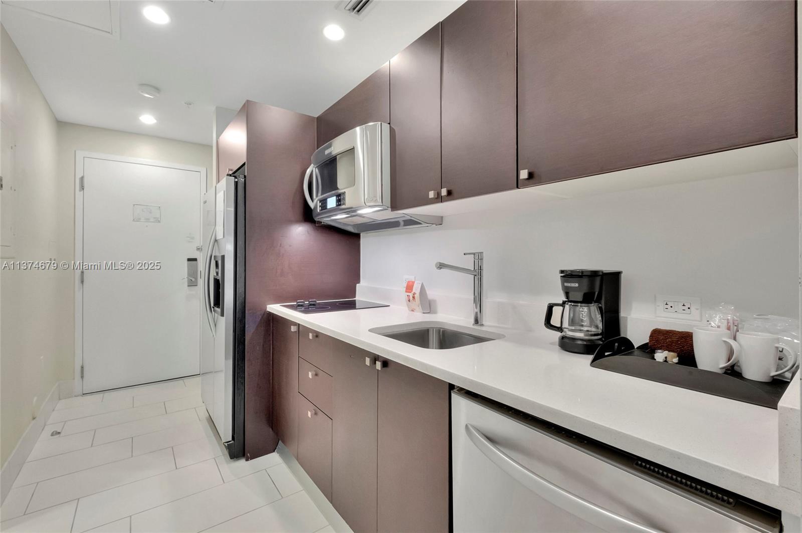 A compact kitchen features dark brown cabinetry, white countertops, stainless steel appliances, and tile flooring — 5300 NW 87th Ave # 606, Doral FL 33178, DORAL, FL
