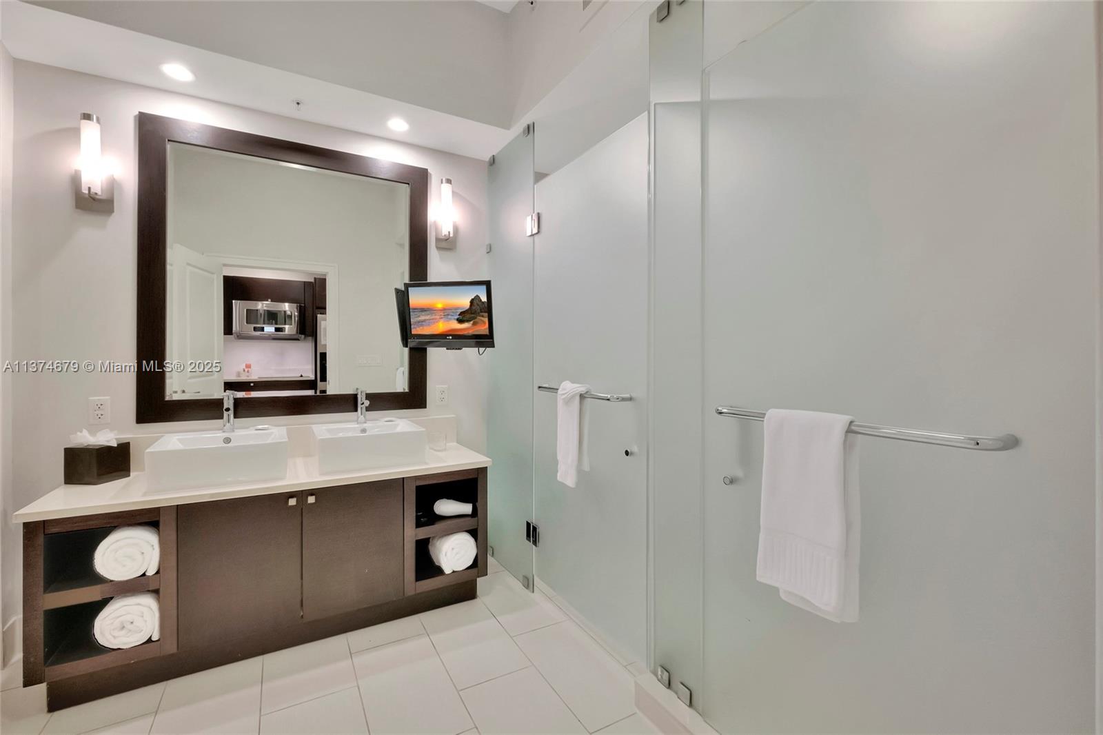 A modern bathroom features a double vanity, frosted glass shower doors, and a wall-mounted television — 5300 NW 87th Ave # 606, Doral FL 33178, DORAL, FL
