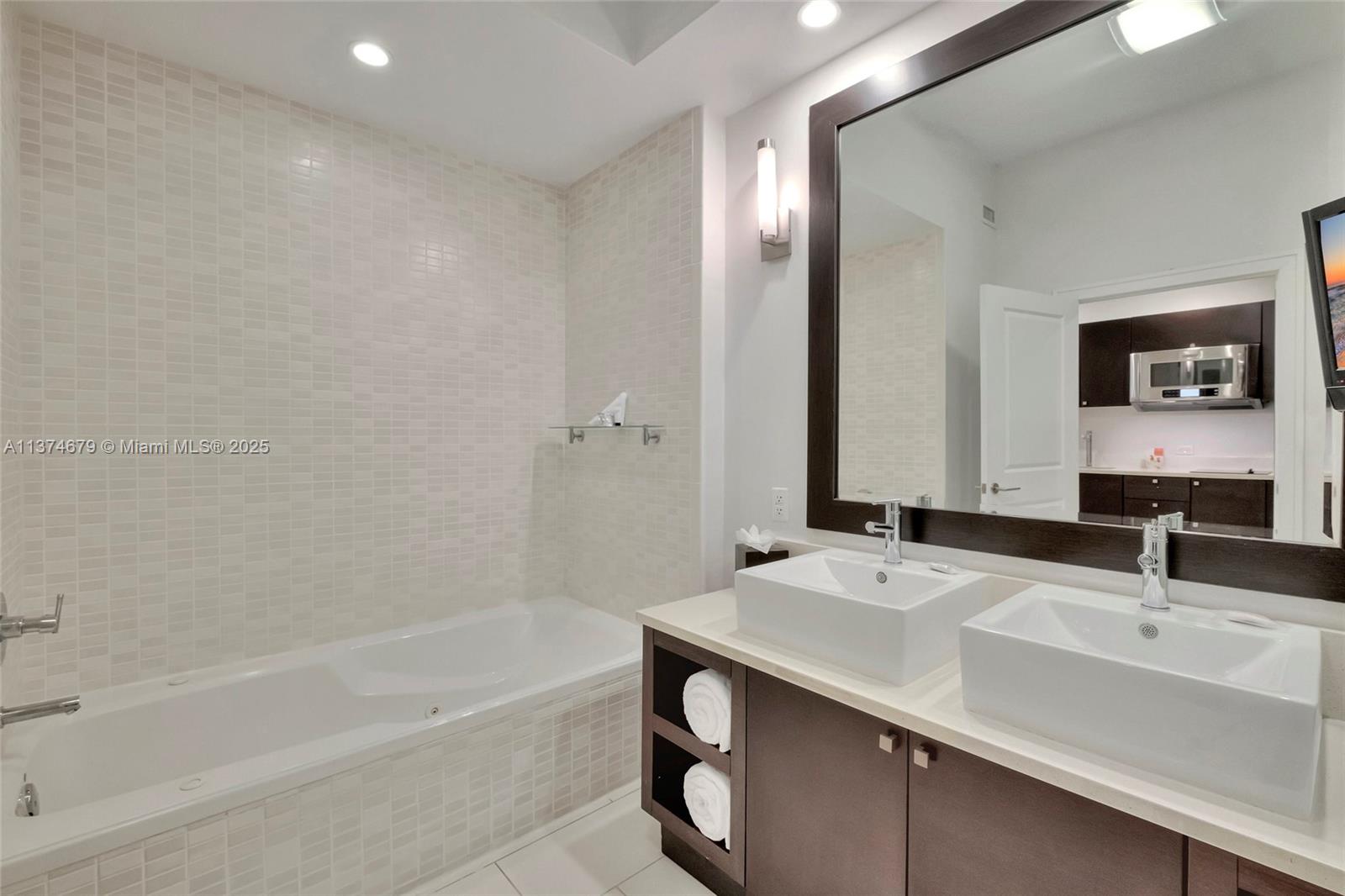 A modern bathroom features a double vanity, a soaking tub, and a large wall mirror — 5300 NW 87th Ave # 606, Doral FL 33178, DORAL, FL