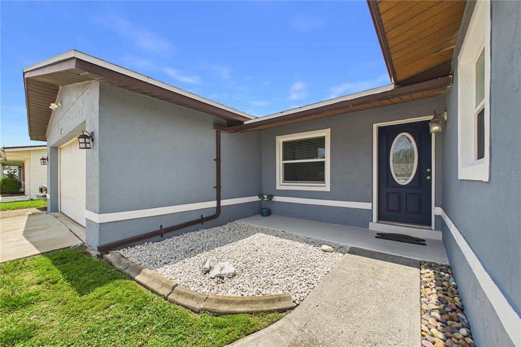 A gray house exterior features a dark blue front door, a garage, and gravel landscaping — 1545 W CORAL COURT, MERRITT ISLAND, FL
