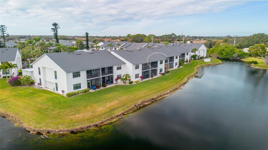 An aerial view shows a multi-story apartment building with screened balconies overlooking a pond — 1100 CAPRI ISLES BOULEVARD UNIT 325, VENICE, FL