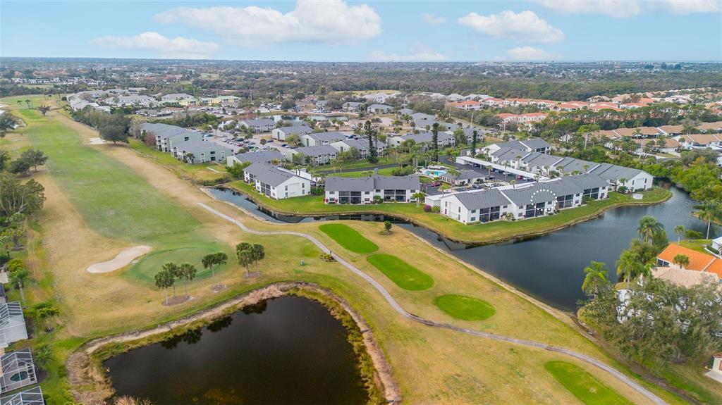 An aerial view shows a multi-story apartment complex situated next to a golf course and pond — 1100 CAPRI ISLES BOULEVARD UNIT 325, VENICE, FL