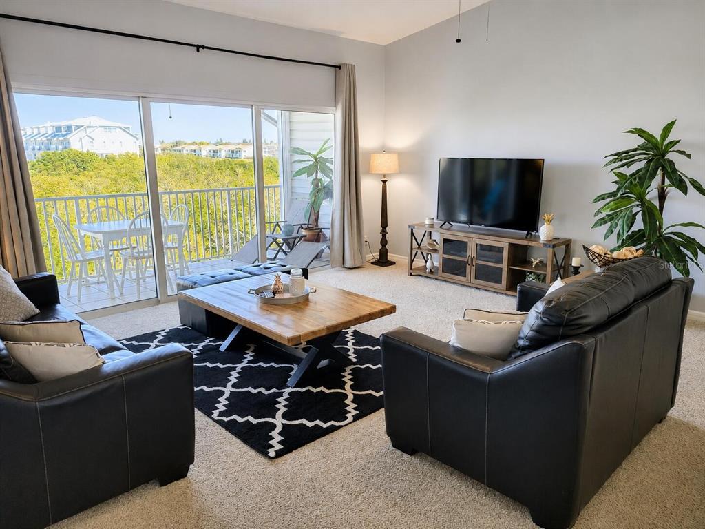 An open-concept living and dining area features a kitchen island, granite countertops, and balcony access — 19829 GULF BOULEVARD UNIT 103, INDIAN ROCKS BEACH, FL