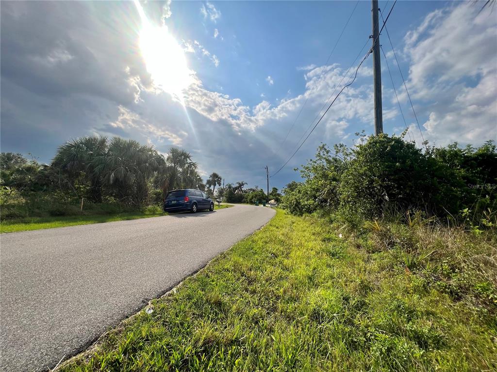 A paved road curves past a parked minivan toward a sunny, tree-lined horizon — 27430 SAN MARCO DRIVE, PUNTA GORDA, FL