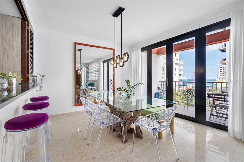 A dining room features a glass-topped driftwood table, clear chairs, and a balcony with ocean views — 1202 Av Magdalena MAGDALENA UNIT 702, SAN JUAN, PR