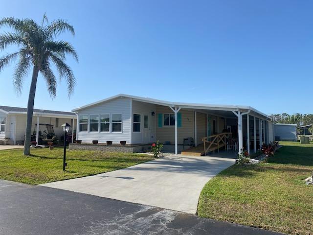 A single-story manufactured home features a concrete driveway, a carport, and a palm tree — 707 DEL LUNA DRIVE, NORTH PORT, FL