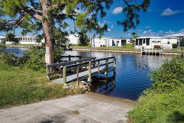 A concrete boat ramp leads to a wooden dock on a canal beside mobile homes — 707 DEL LUNA DRIVE, NORTH PORT, FL