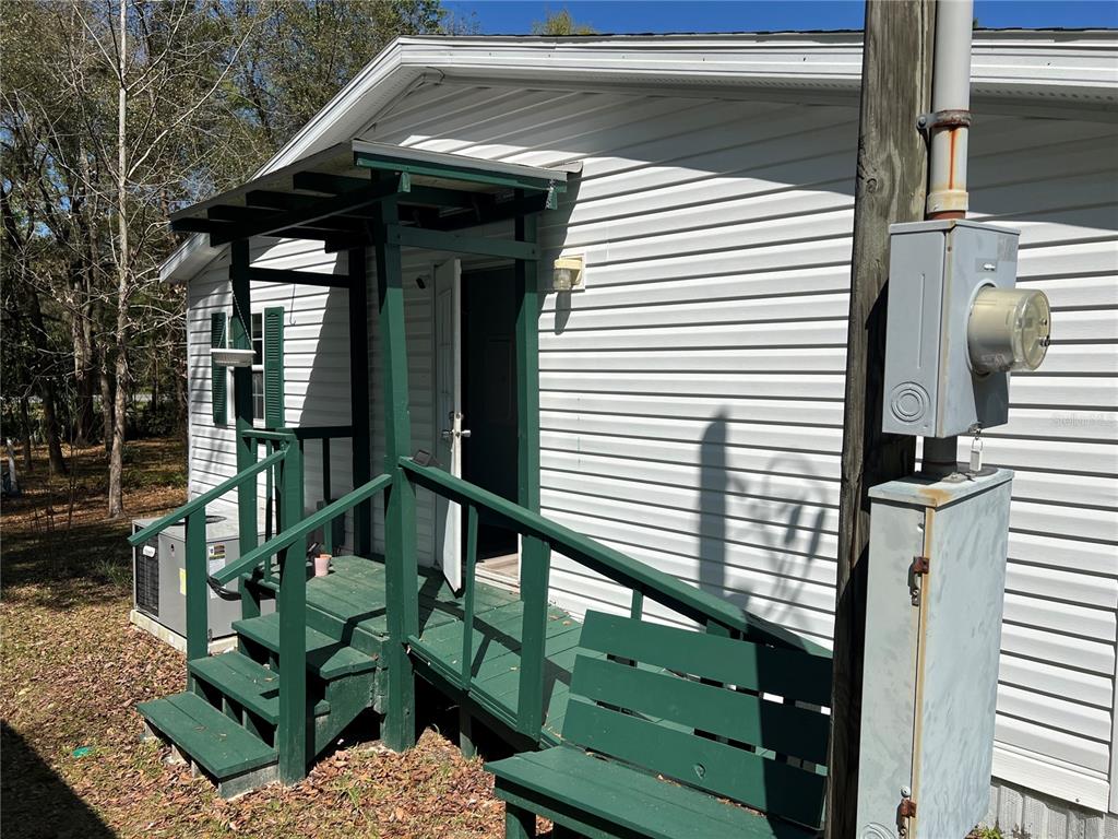 A white vinyl-sided house exterior features a green wooden porch, stairs, and an electrical meter — 15926 NE 13TH STREET, WILLISTON, FL