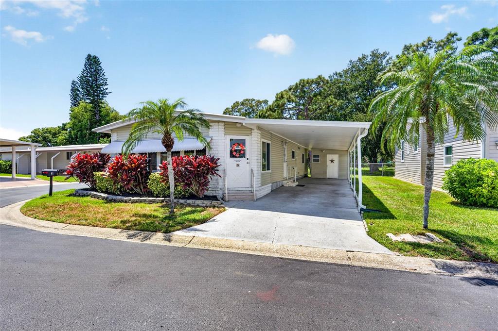 A single-story manufactured home features a carport, palm trees, and red landscaping plants — 12501 ULMERTON ROAD UNIT 5, LARGO, FL