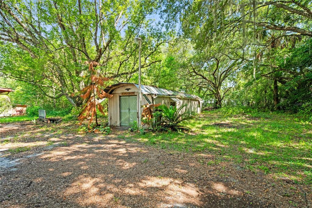 A long, light-colored shed with double doors sits in a wooded, grassy yard — 140 W PONKAN ROAD, APOPKA, FL
