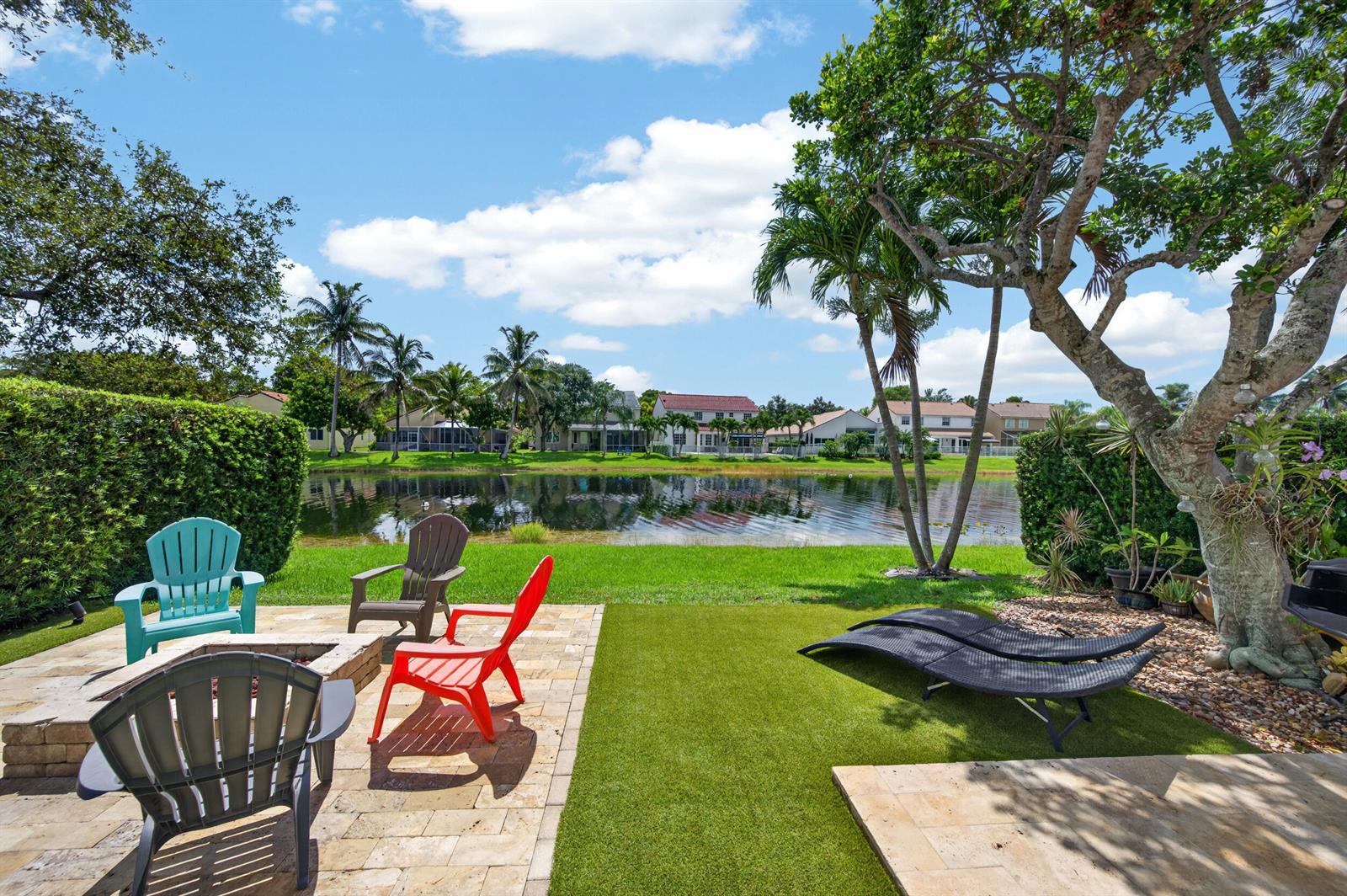 A backyard patio with a fire pit, several chairs, and lounge chairs overlooking a lake — 229 E Bayridge Drive, Weston FL 33326, WESTON, FL