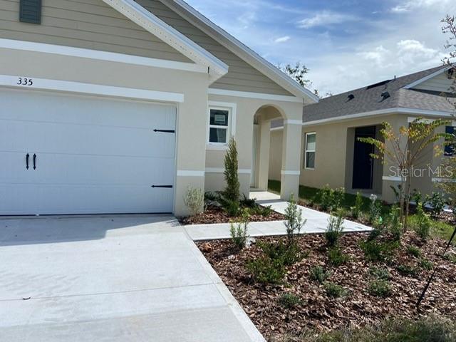 A tan house exterior features a white garage door, a concrete driveway, and landscaped mulch — 335 GINA LANE, DAVENPORT, FL