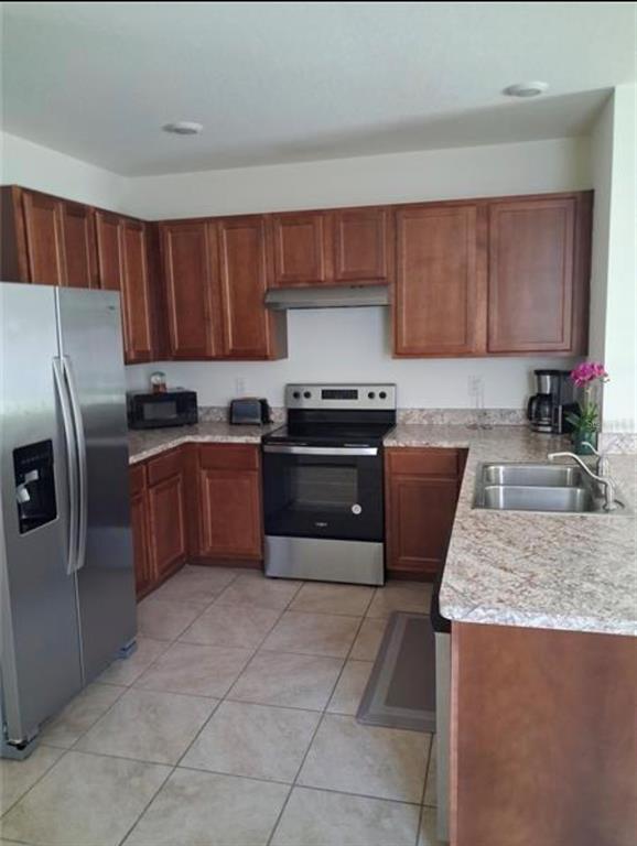 A kitchen features wood cabinets, stainless steel appliances, and granite countertops over tile flooring — 335 GINA LANE, DAVENPORT, FL