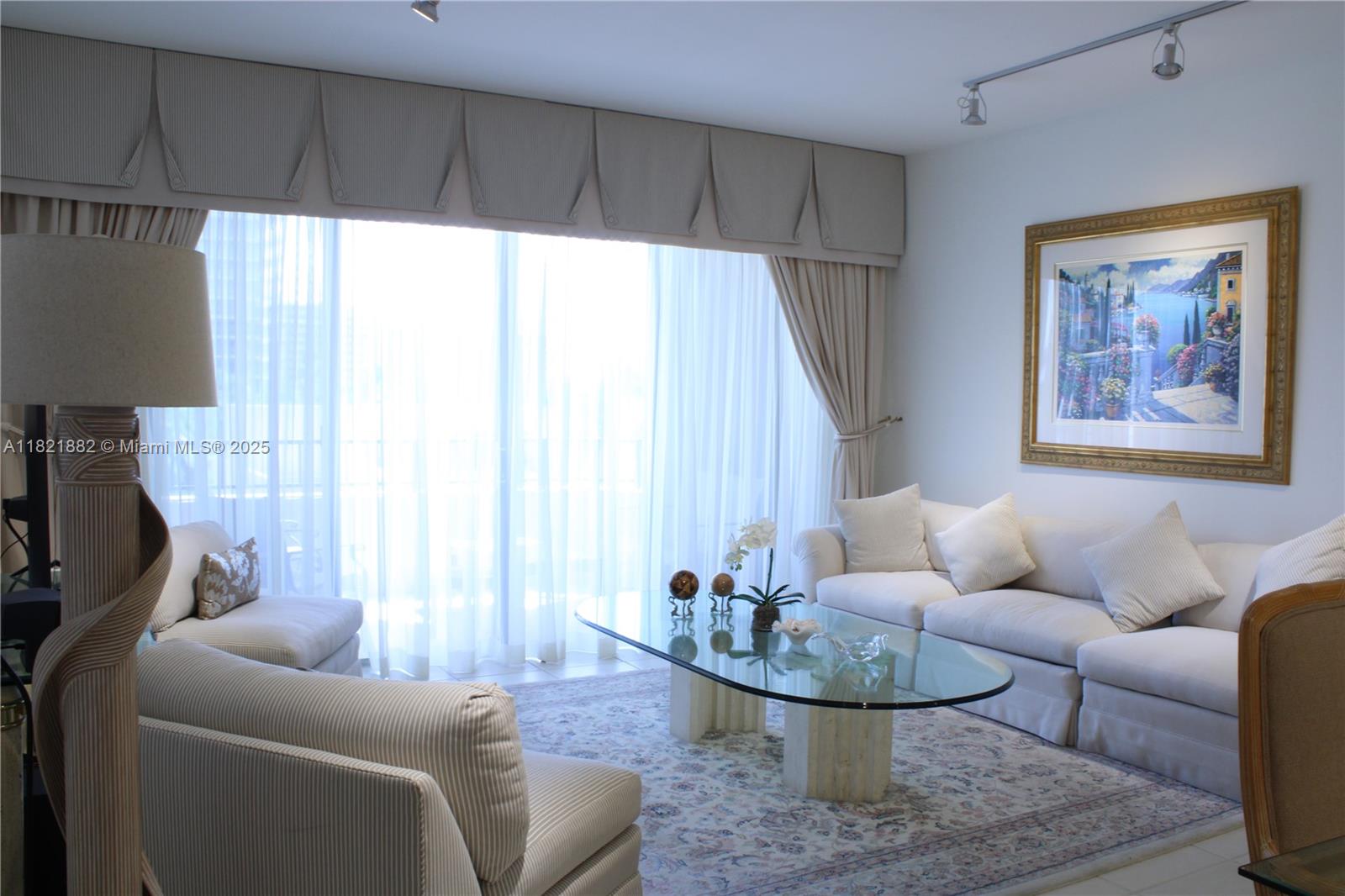 A living room features a white sofa, glass coffee table, patterned rug, and floor-to-ceiling curtains — 201 Crandon Blvd # 439, Key Biscayne FL 33149, KEY BISCAYNE, FL