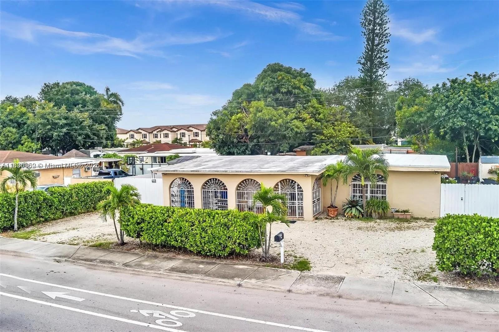 A single-story house with arched windows and a gravel front yard sits behind a hedge — 12840 NW 22nd Ave, Miami FL 33167, MIAMI, FL