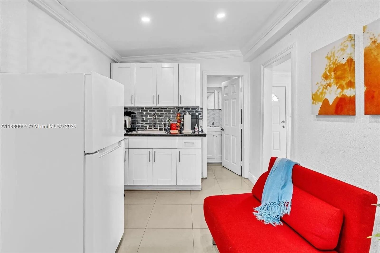 A small kitchen with white cabinets and a red sofa in the foreground — 12840 NW 22nd Ave, Miami FL 33167, MIAMI, FL