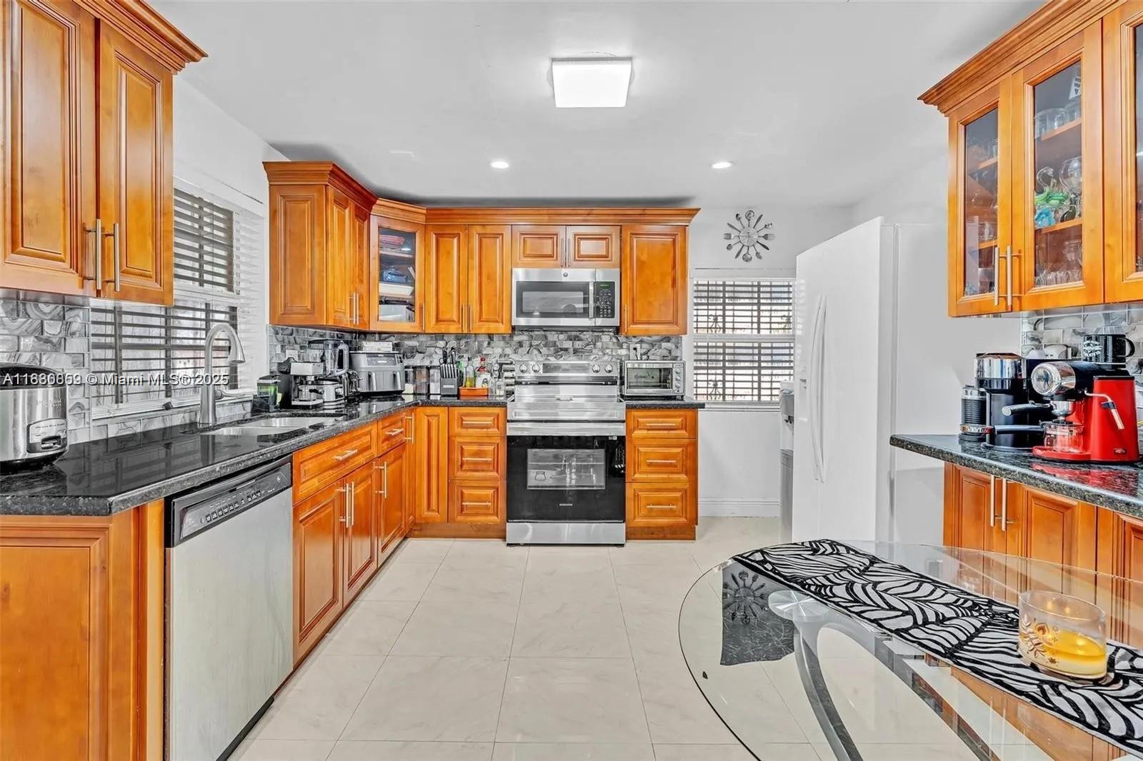 A kitchen features wooden cabinets, black granite countertops, stainless steel appliances, and light tile flooring — 12840 NW 22nd Ave, Miami FL 33167, MIAMI, FL