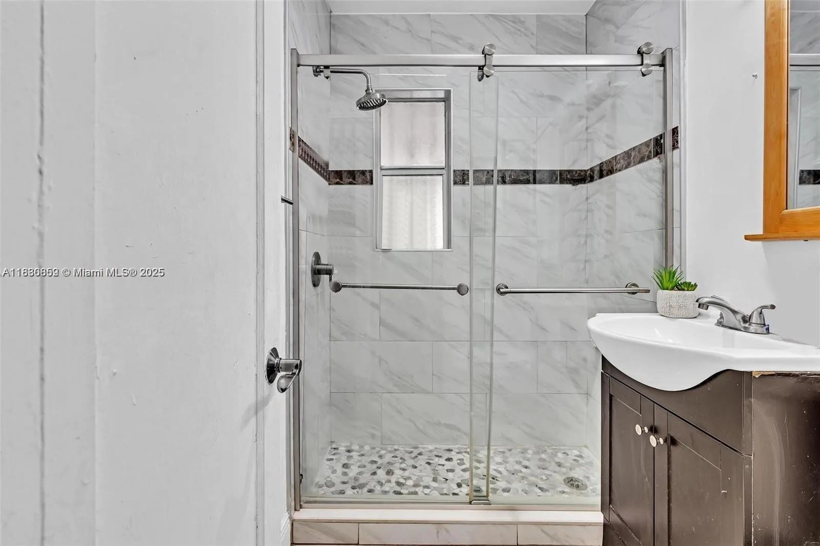 A bathroom features a glass-enclosed shower with marble-look tile, a pebble floor, and a vanity — 12840 NW 22nd Ave, Miami FL 33167, MIAMI, FL