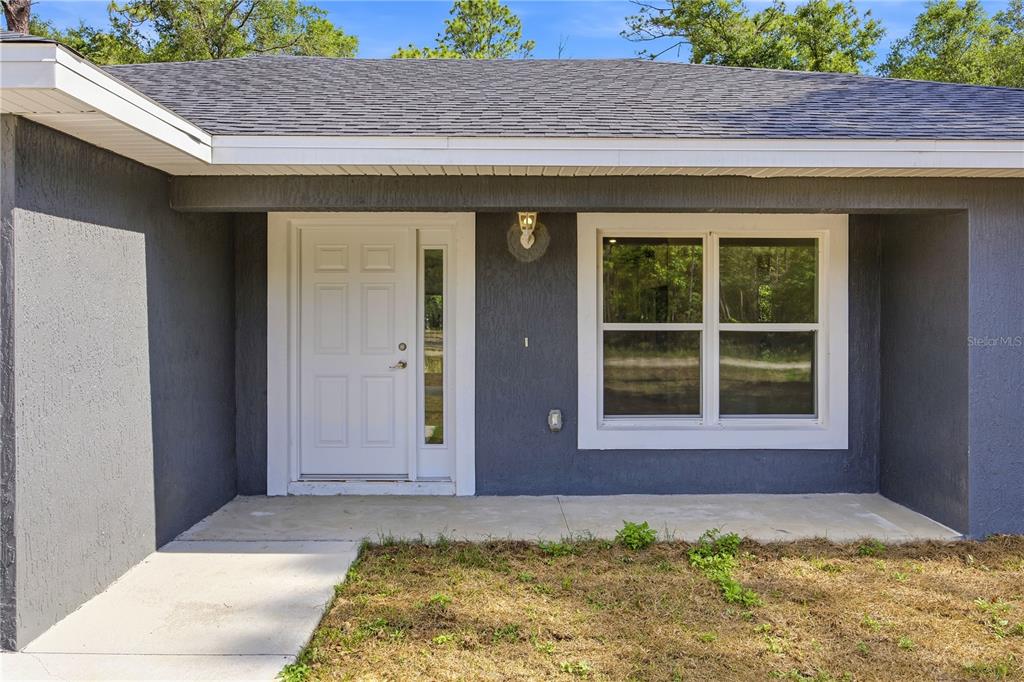 A gray house exterior features a white front door with a sidelight and a window — 15649 SW 40TH STREET, OCALA, FL