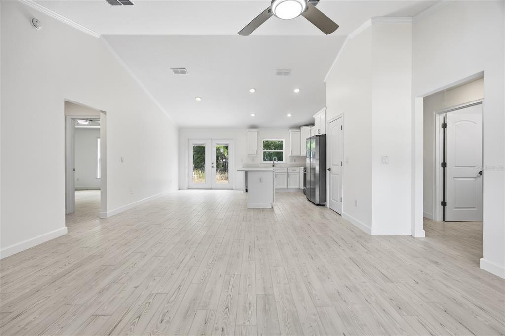 A bright, open-concept kitchen and living area featuring white cabinetry, light wood-look flooring, and vaulted ceilings — 15649 SW 40TH STREET, OCALA, FL