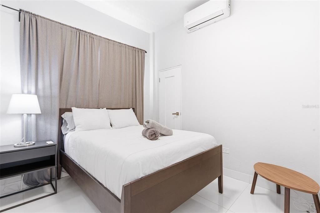 A bedroom features a wooden bed frame, white bedding, a nightstand, and a wall-mounted air conditioner — 56 CALLE F KRUG CONDADO UNIT 6, SAN JUAN, PR
