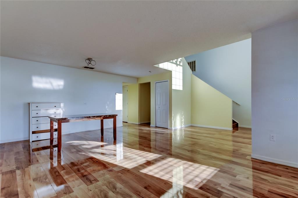 An empty room features hardwood flooring, a white dresser, a wooden table, and a staircase — 11309 OUTRIGGER AVENUE, SPRING HILL, FL