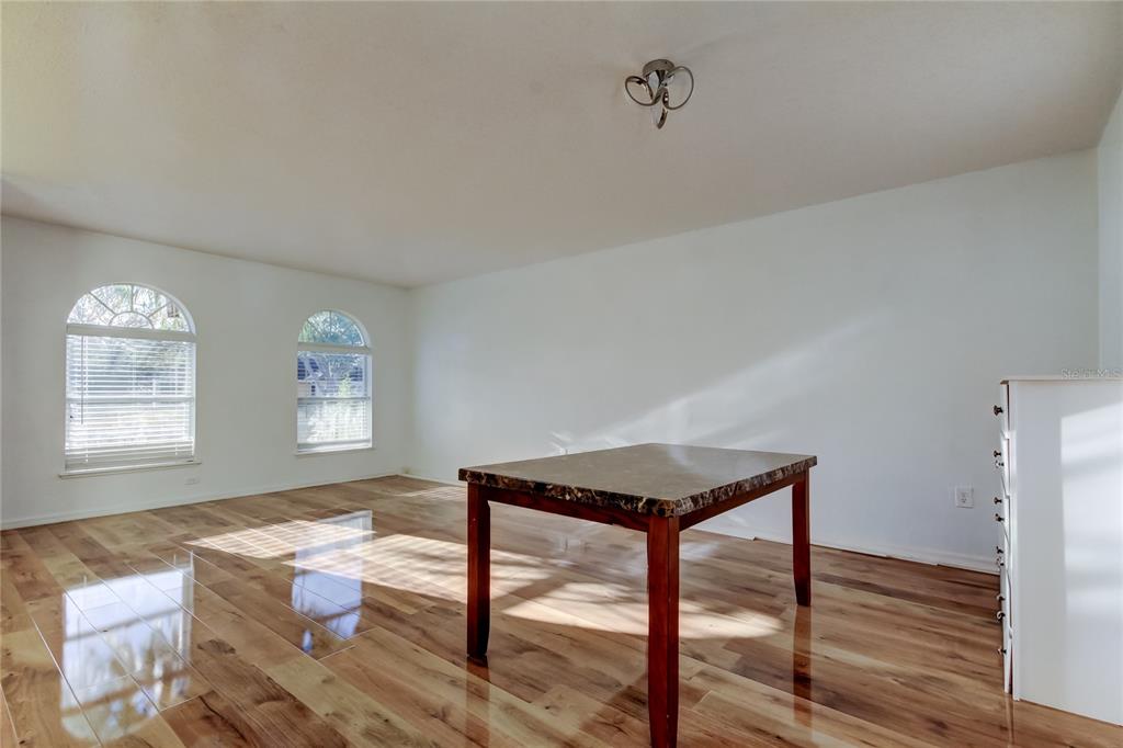 A dining room with light wood floors, white walls, two arched windows, and a marble-topped table — 11309 OUTRIGGER AVENUE, SPRING HILL, FL
