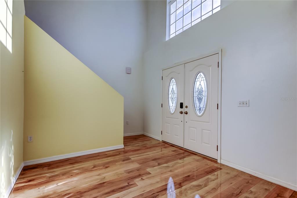 An entryway with wood-look flooring, a yellow accent wall, and double doors with glass inserts — 11309 OUTRIGGER AVENUE, SPRING HILL, FL