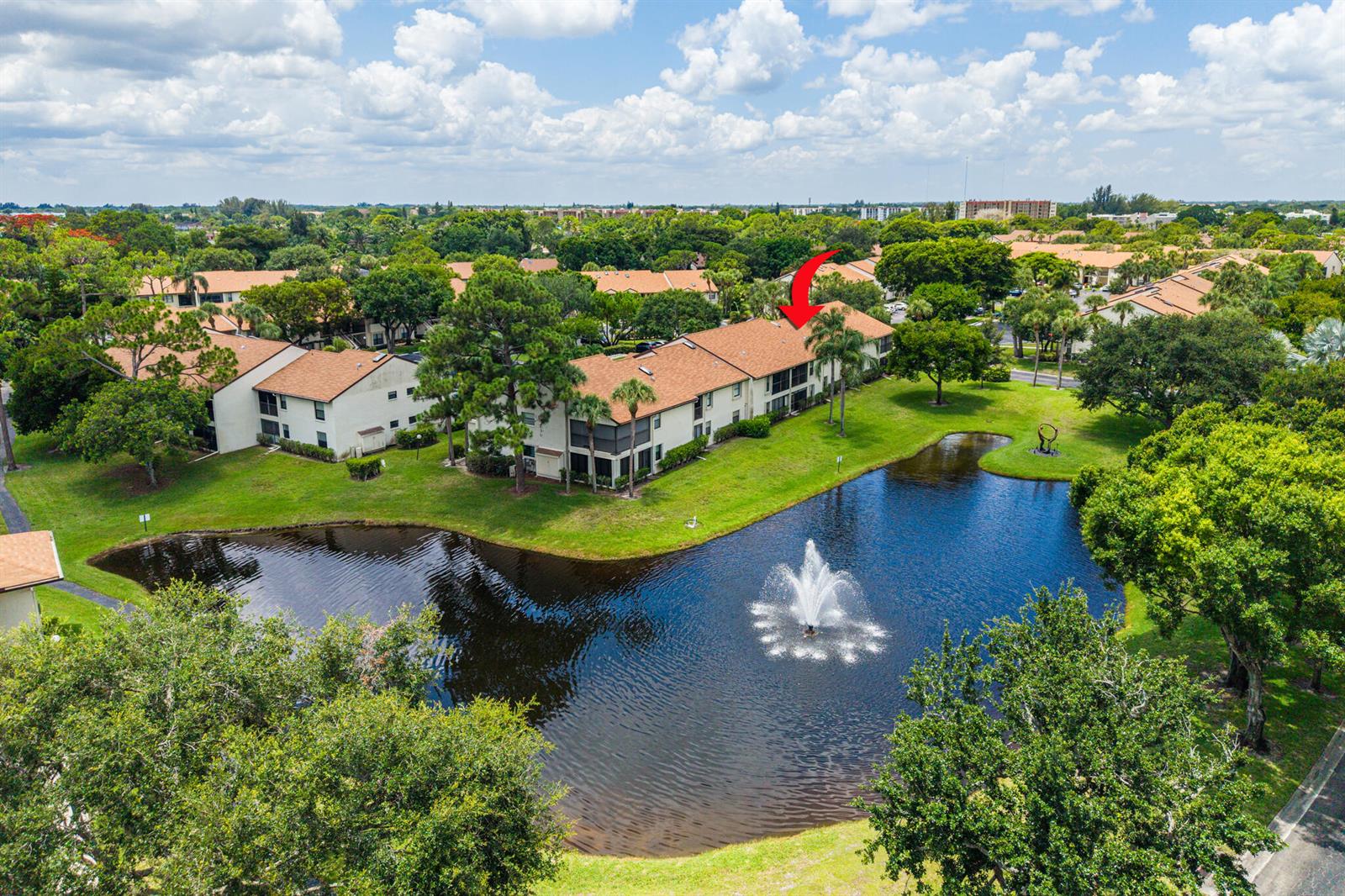 An aerial view shows a multi-story apartment building beside a pond with a fountain — 3386 Lucerne Park Drive, FL 33467, FL