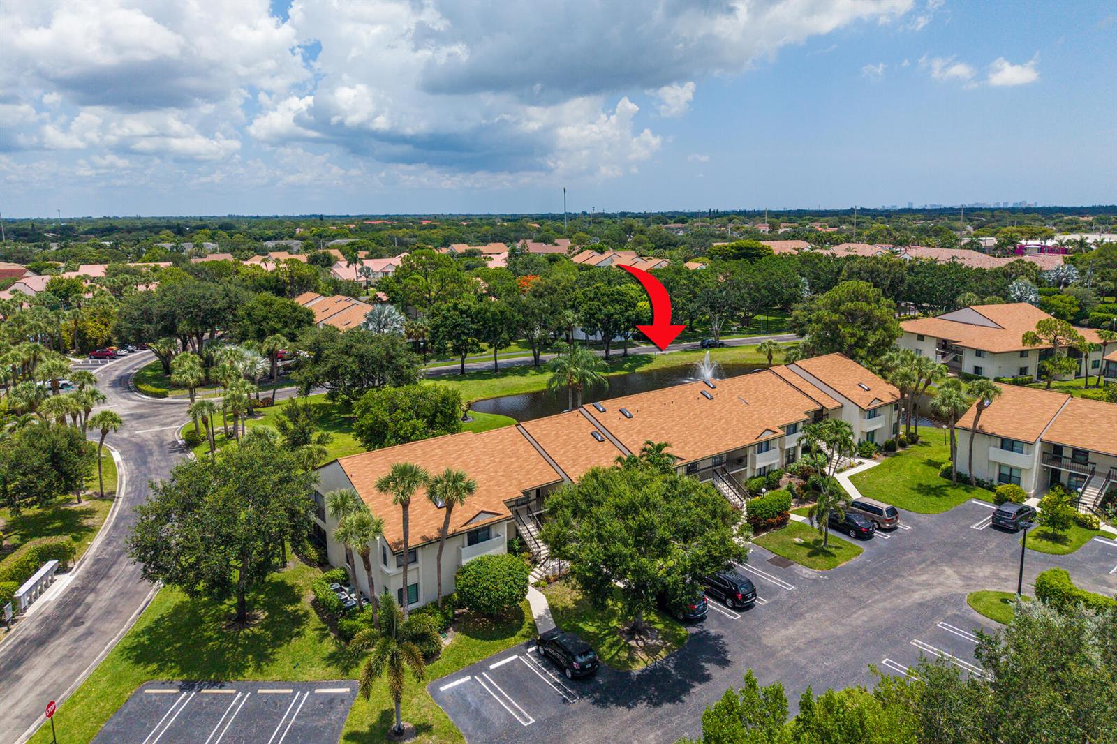 An aerial view shows multi-story apartment buildings with brown roofs surrounding a small pond — 3386 Lucerne Park Drive, FL 33467, FL