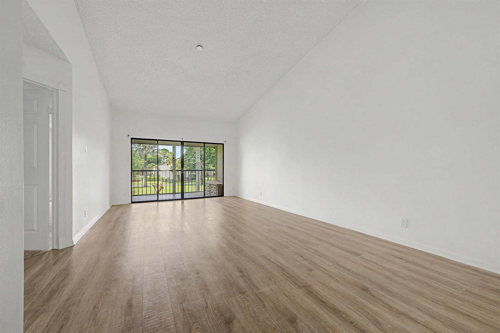 An empty living room features white walls, wood-look flooring, and sliding glass doors to a balcony — 3386 Lucerne Park Drive, FL 33467, FL