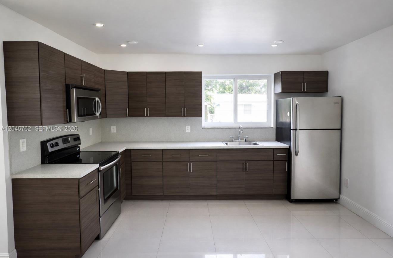 A kitchen features dark wood cabinets, stainless steel appliances, white countertops, and light tile flooring — 552 NE 61st St # 4, Miami FL 33137, MIAMI, FL