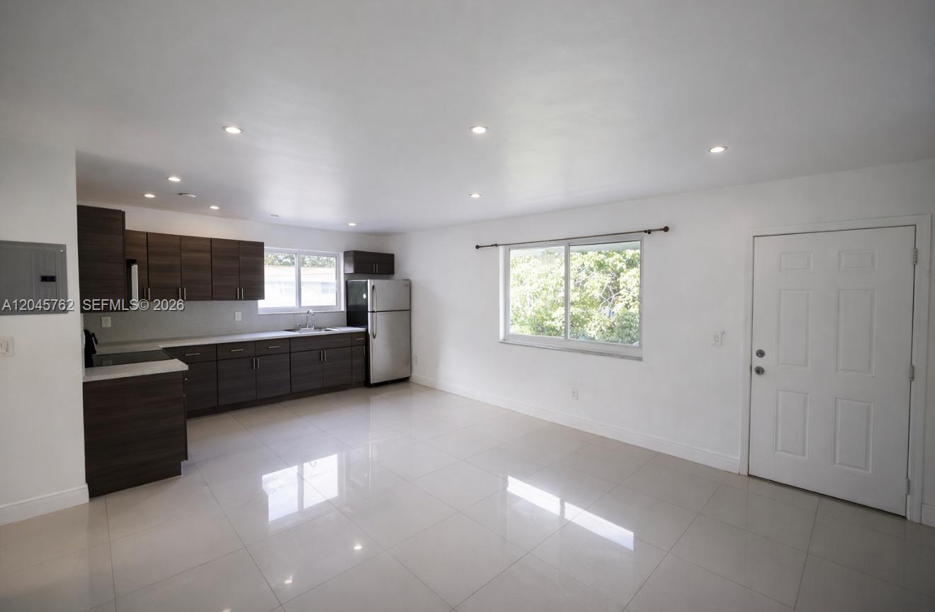 A kitchen with dark wood cabinets and stainless steel appliances opens into a tiled living area — 552 NE 61st St # 4, Miami FL 33137, MIAMI, FL