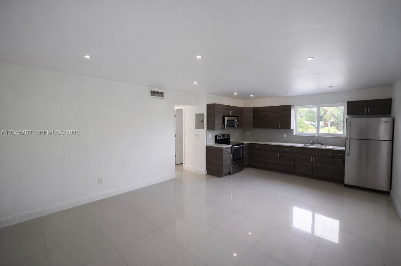 A kitchen with dark wood cabinets and stainless steel appliances opens to a living area — 552 NE 61st St # 4, Miami FL 33137, MIAMI, FL