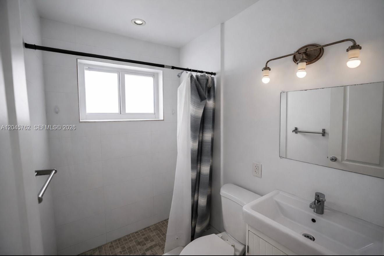 A small bathroom features a tiled walk-in shower, a pedestal sink, and a vanity mirror — 552 NE 61st St # 4, Miami FL 33137, MIAMI, FL